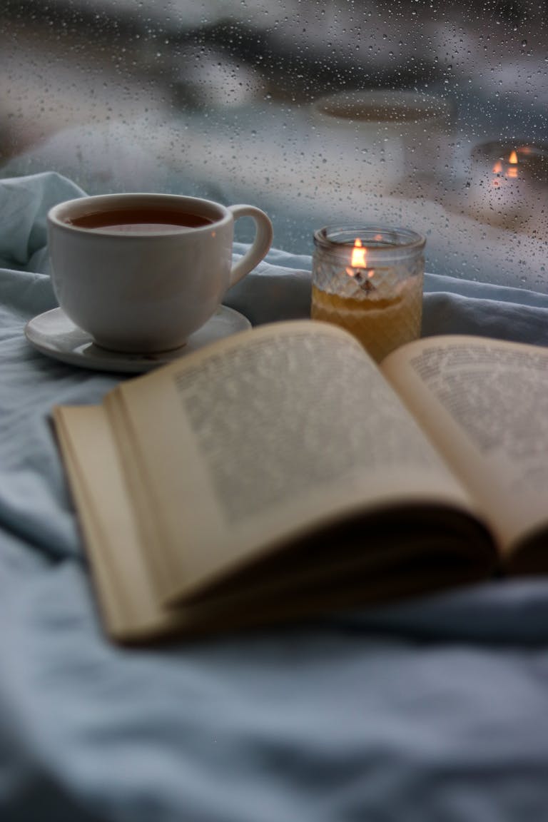 Taza sobre una mesa junto a un libro abierto y una vela encendida, en un interior con luz tenue.