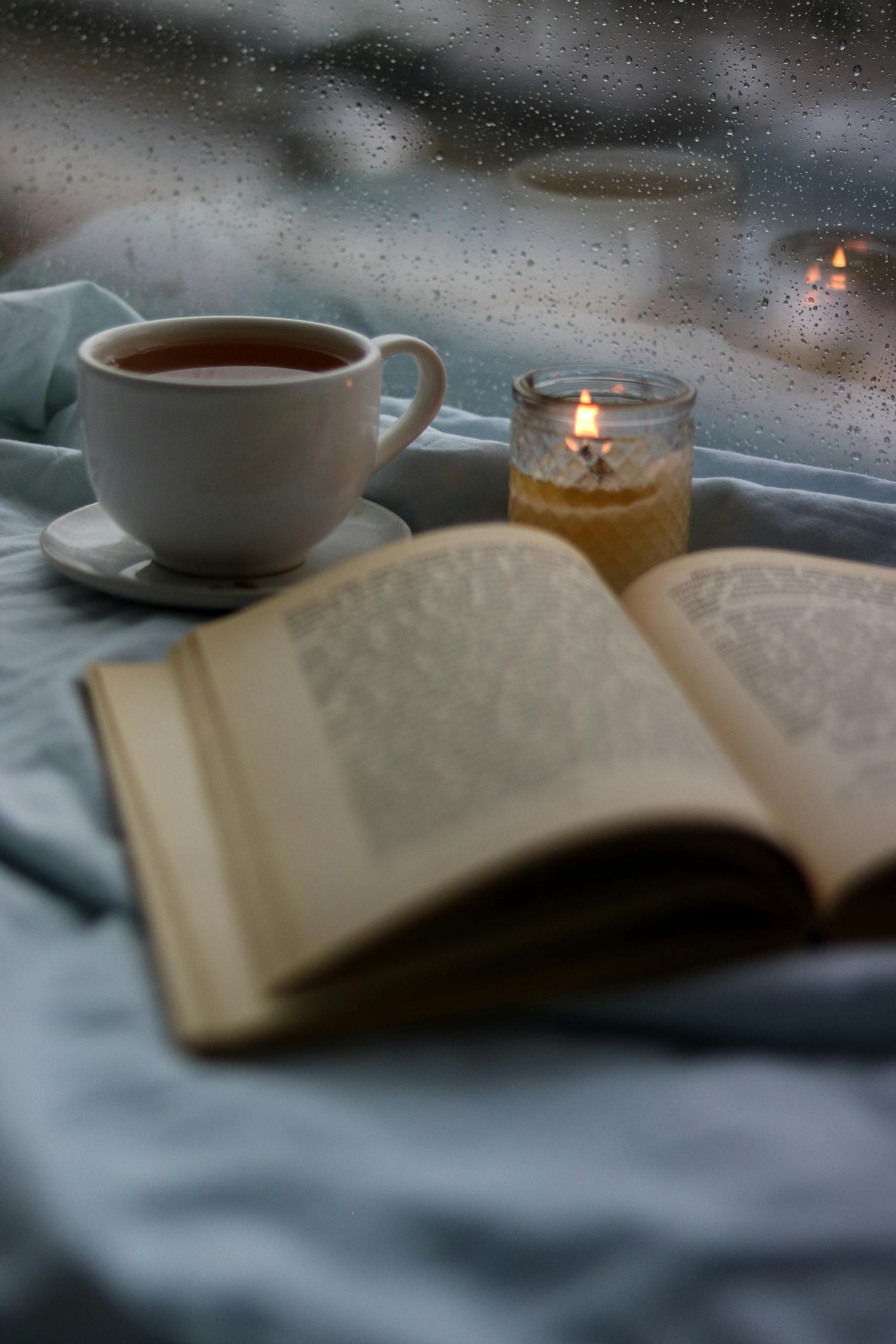 Taza sobre una mesa junto a un libro abierto y una vela encendida, en un interior con luz tenue.