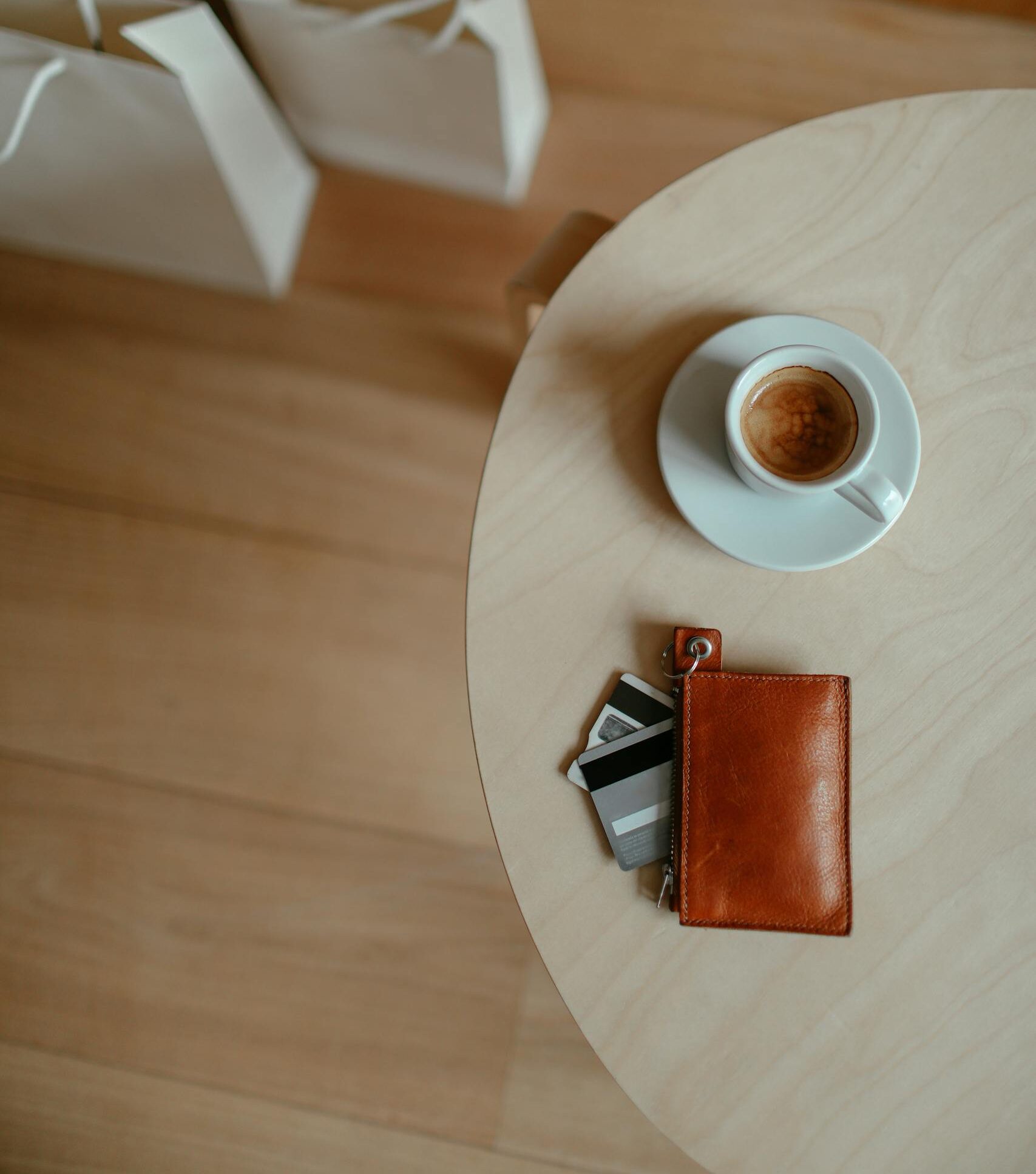 Vista superior de una taza de café sobre una mesa de madera, junto a una cartera y tarjetas, en una escena cotidiana y ordenada.