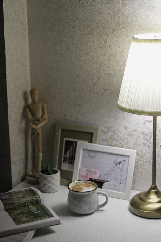 Mesa auxiliar con lámpara encendida, taza de café, marcos y una revista abierta en un rincón interior con luz cálida