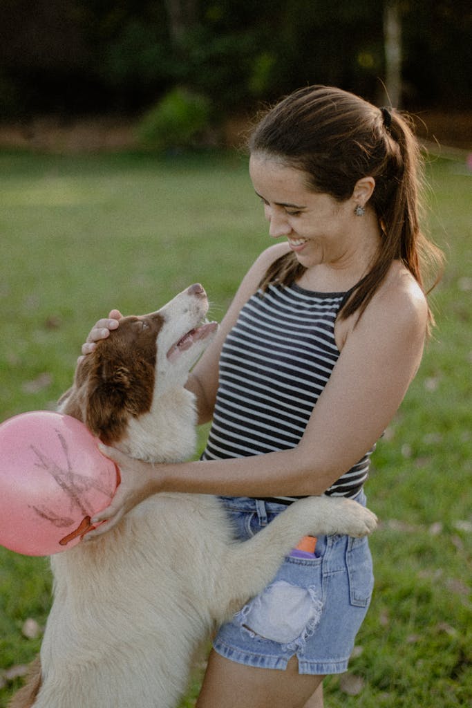 Mujer sonriendo mientras abraza y juega con su perro al aire libre.