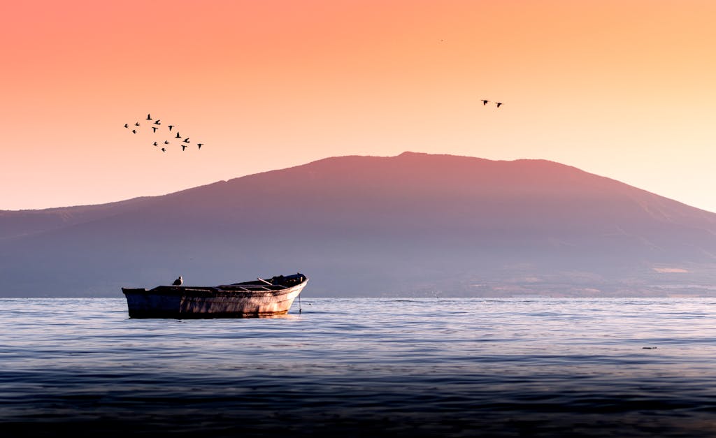 Amanecer tranquilo sobre el Lago de Chapala, Jalisco, México, con una lancha solitaria y montañas al fondo.