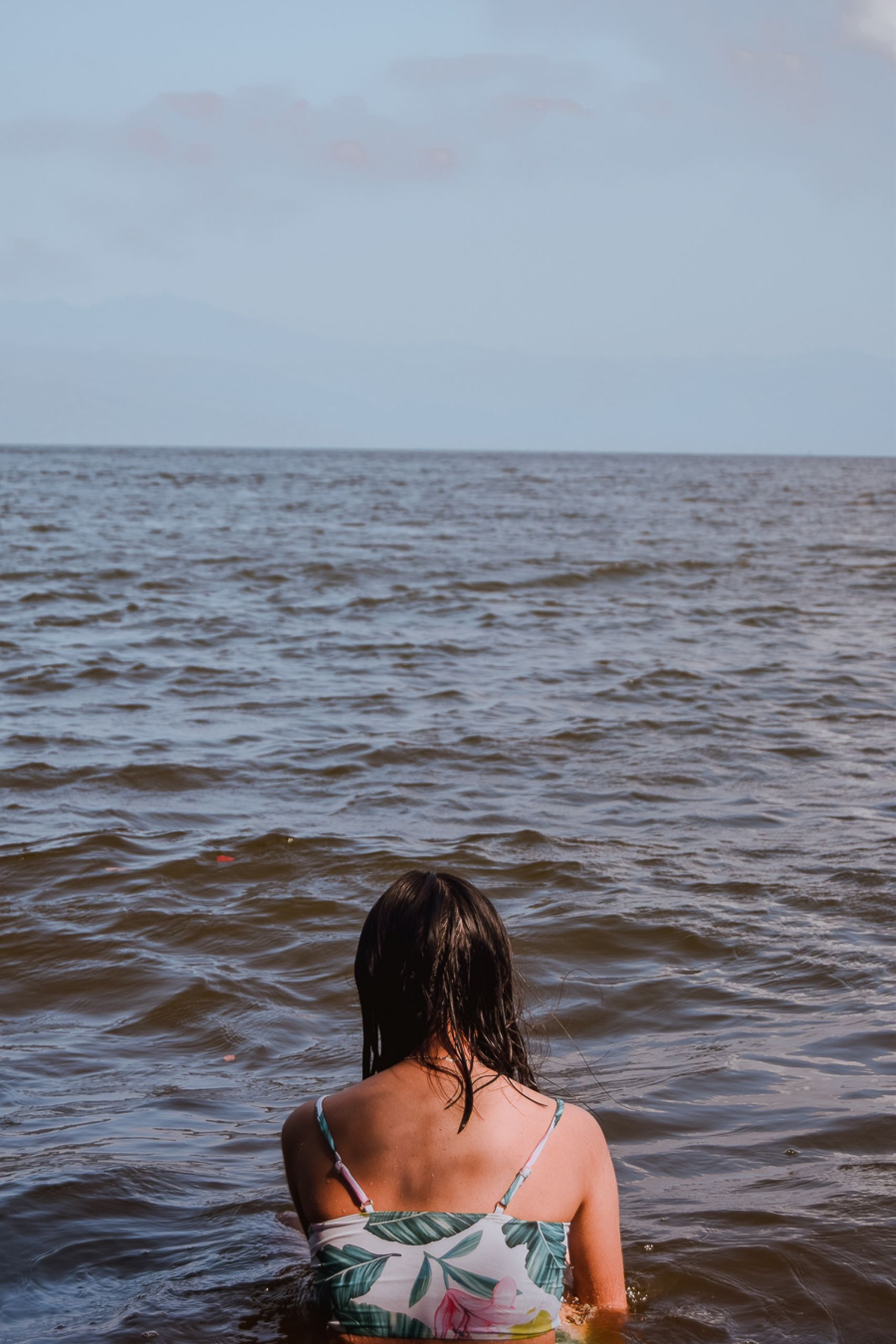 Back view of a woman in the ocean enjoying solitude under a clear sky.