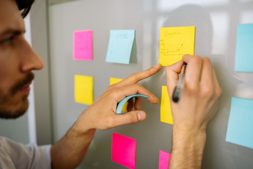 Persona organizando notas adhesivas en una pared para representar pensamiento interconectado y búsqueda de patrones.