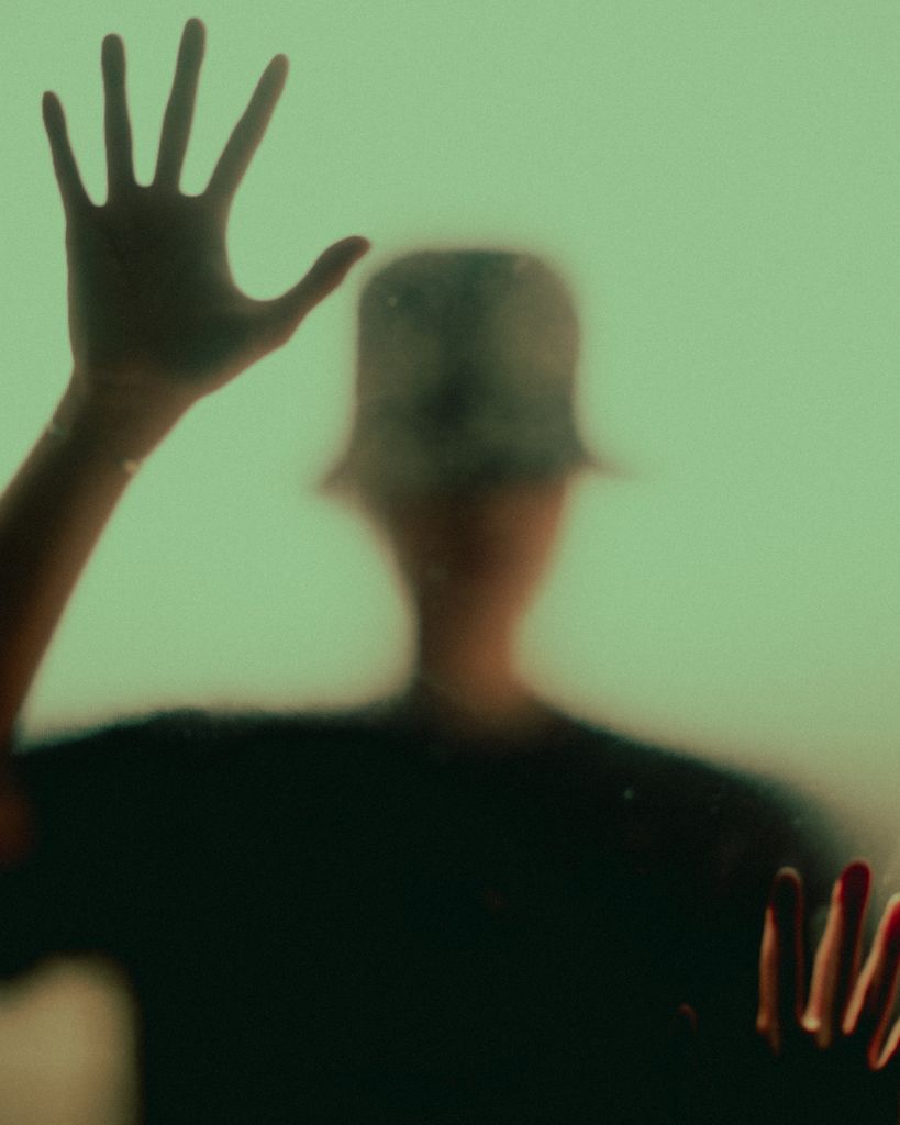 Silueta de una persona detrás de un cristal, con la mano apoyada sobre la superficie.
