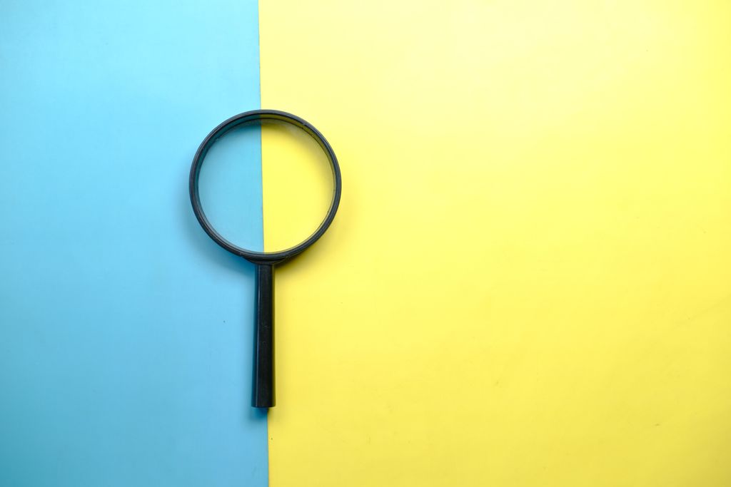 Lupa sobre un fondo dividido en azul y amarillo, como símbolo de análisis, contraste y verificación de información.
