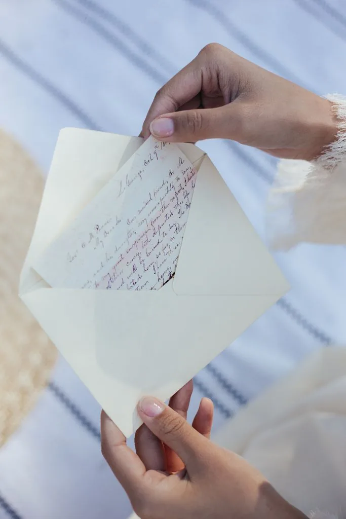 Manos abriendo un sobre con una carta escrita a mano.