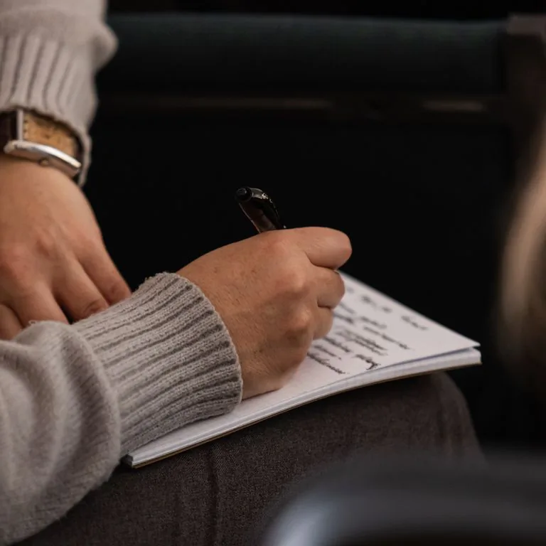 Persona escribiendo en una libreta, imagen asociada a un artículo sobre síndrome del impostor, logros y aprendizaje.