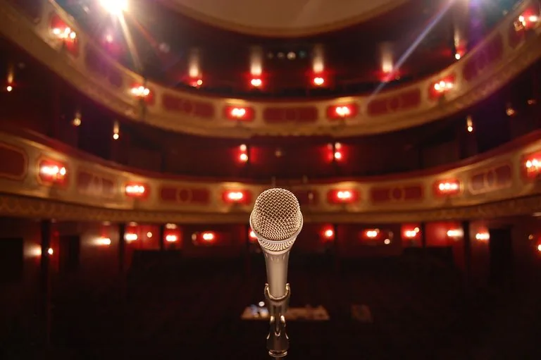 Micrófono frente a un teatro vacío iluminado, como símbolo de la duda antes de exponerse ante los demás.