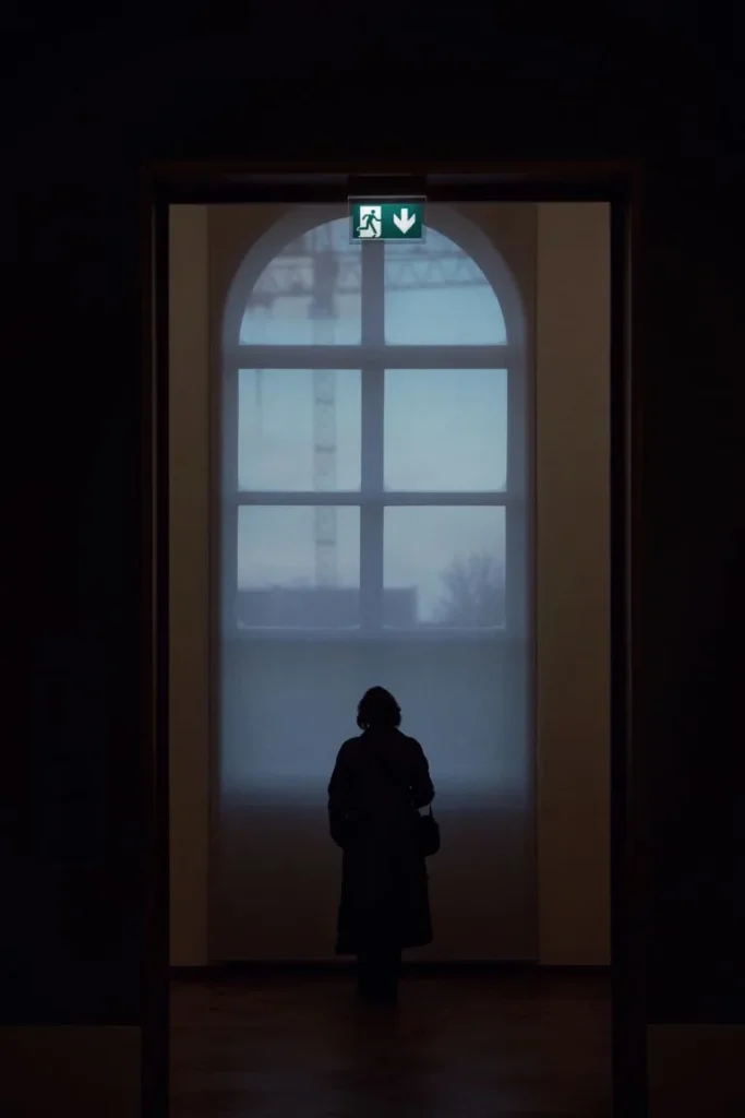 Persona de pie frente a una abertura iluminada, imagen que acompaña un artículo sobre síndrome del impostor y dudas sobre la propia capacidad.